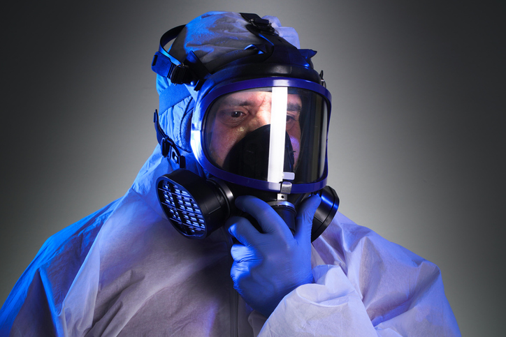 A man wearing a protective suit equipped with a Powered Air-Purifying Respirator for safety.